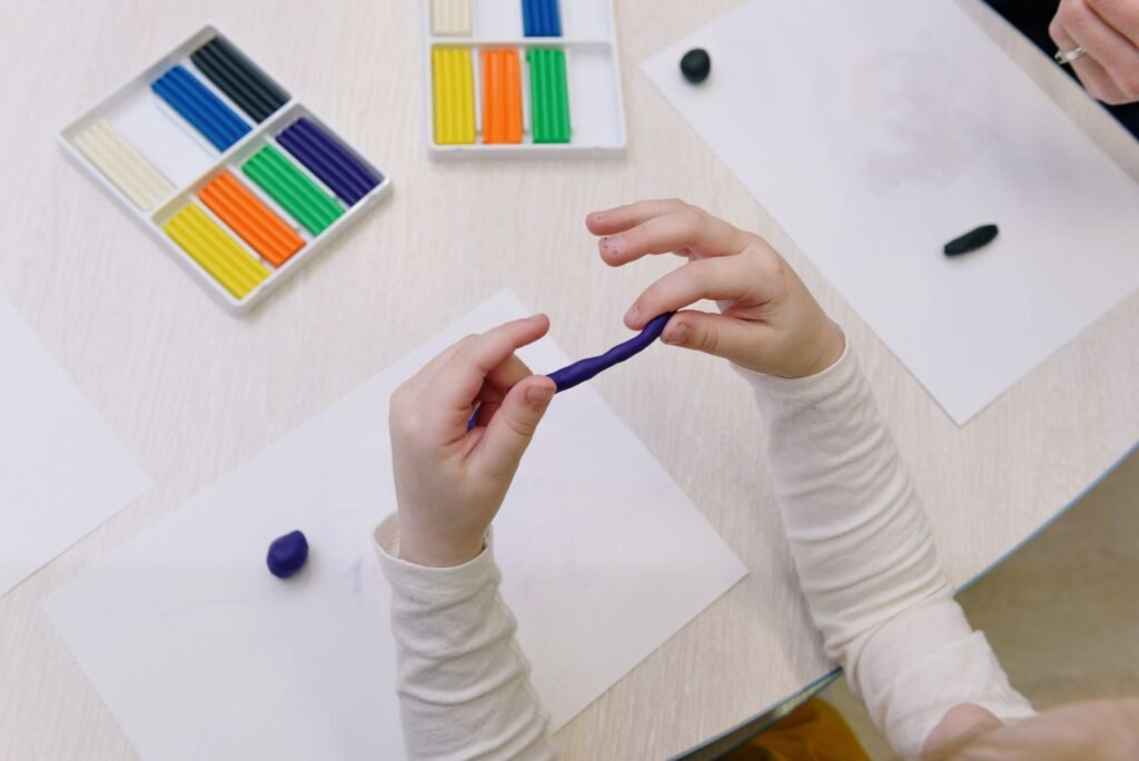 Kinderhände formen bunte Modelliermasse am Basteltisch